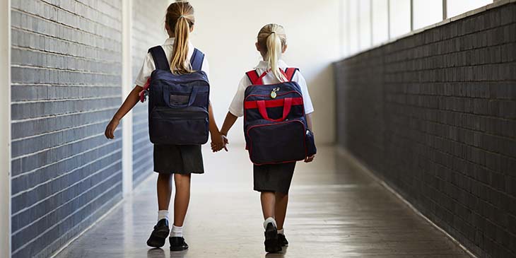 2 young children holding hands walking down a school corridor